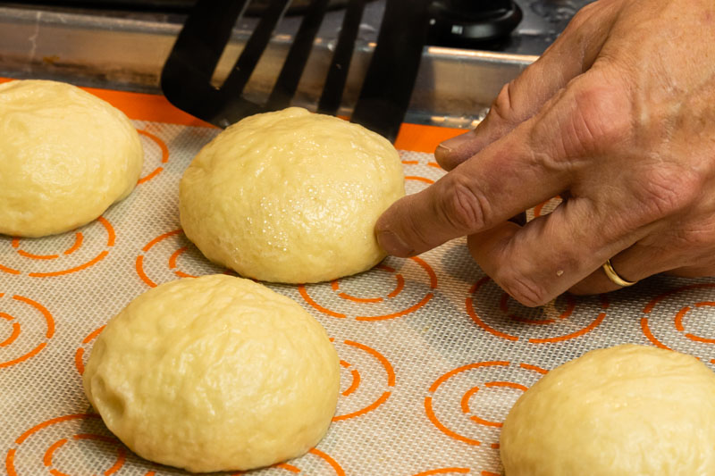 Pretzel buns being placed on a silicone baking pad after the baking soda water bath