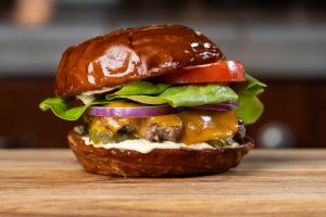 Cheeseburger with lettuce, tomato, onions, pickles, and cheeseburger sauce on a pretzel roll