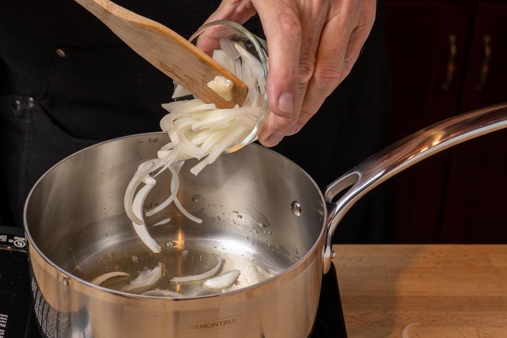 Adding sliced onions to a stainless steel pan