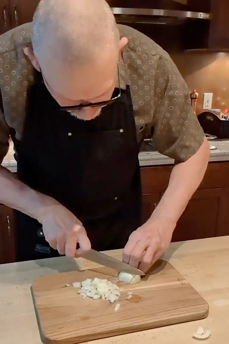 Cheeseburger Guru dicing an onion with a chef's knife on a wooden cutting board