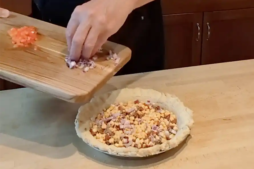 Adding onions and bell peppers to a pie crust.