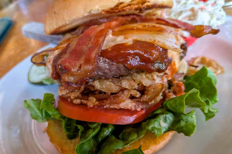 Close-up of a cheeseburger showing the lettuce, tomato, crispy onions, beef patty, sauces, cheese, bacon and the bun