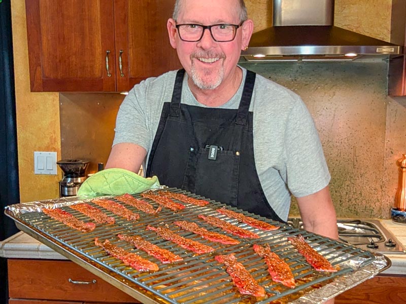 Cheeseburger Guru holding a sheet pan with cooked candied bacon